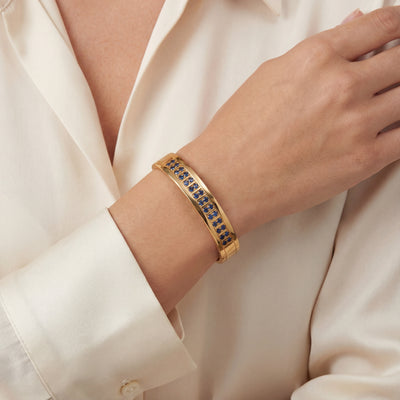 Armreif Gold 585 mit blauen Saphiren am Handgelenk einer hell bekleideten Dame
